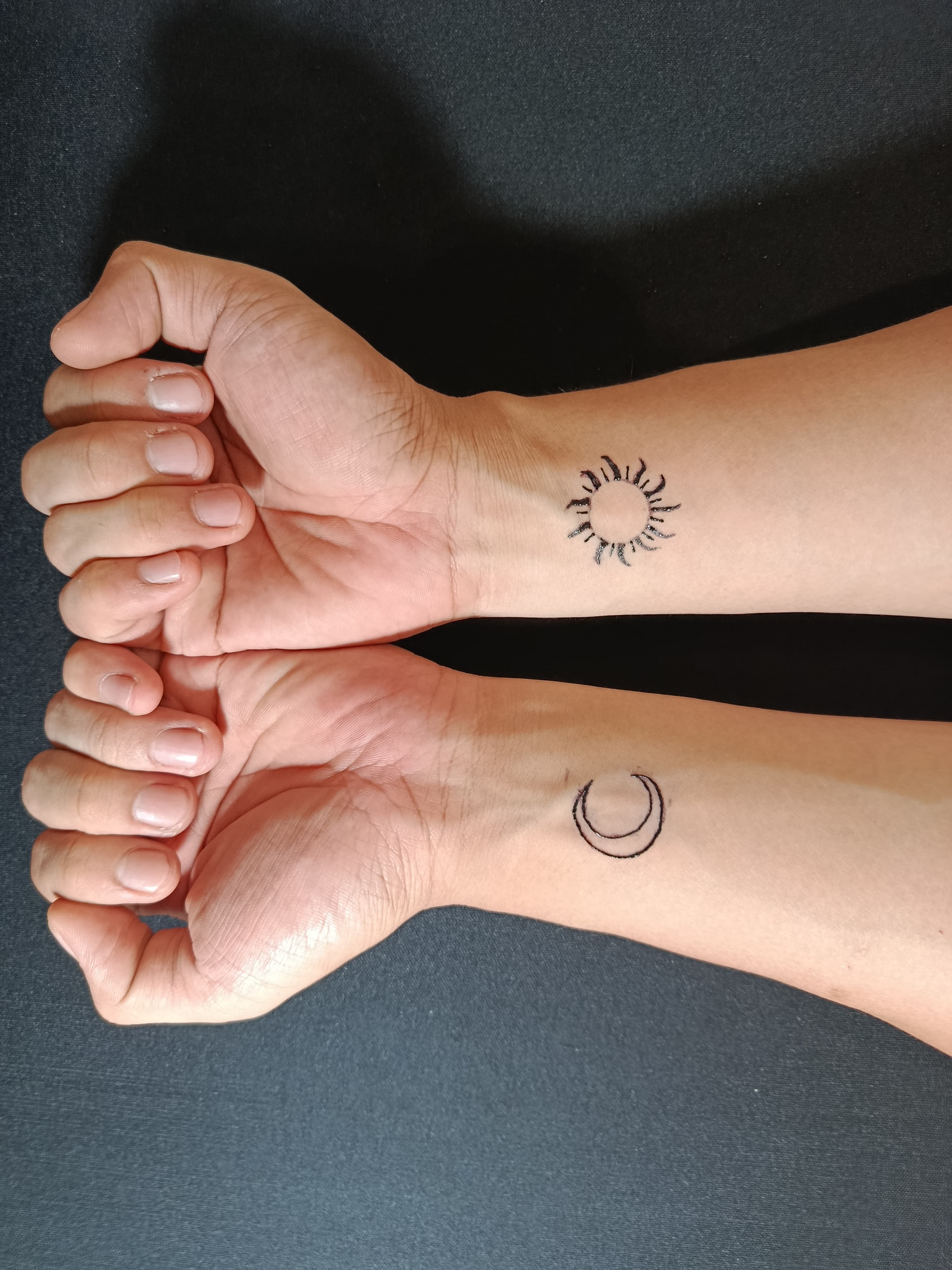 Two wrists with complementary sun and crescent moon tattoos