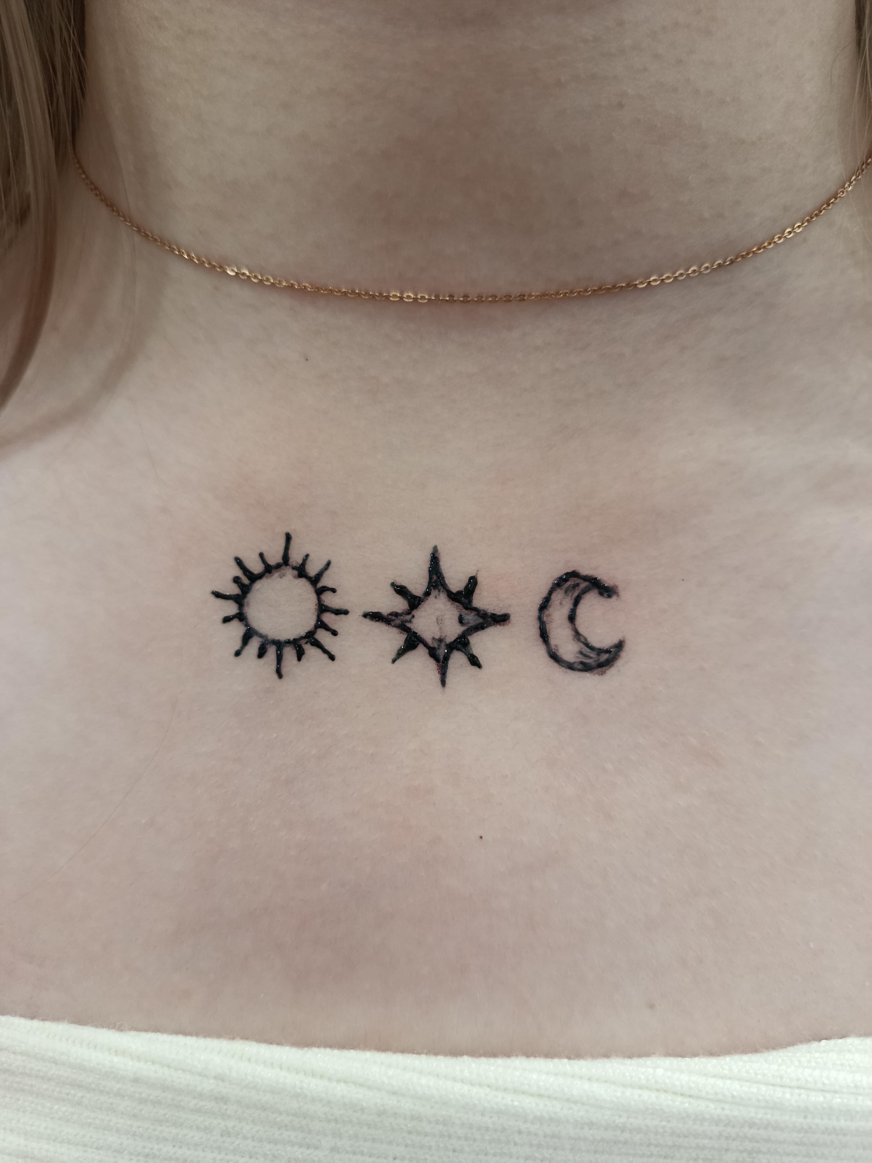 Sun, star, and crescent moon tattoos below the collarbone